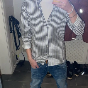 Randig skjorta med knappar - Snygg J.Lindeberg randig skjorta med knappar och långärmad design. Perfekt för en stilren look. Skjortan har en klassisk krage och är i en slim fit passform.