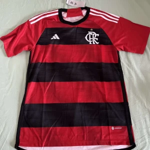 CRF FOTBOLLSTRÖJA  - Snygg fotbollströja från Adidas i röd och svart med vita detaljer. Tröjan har korta ärmar och ett randigt mönster. Perfekt för fotbollsfans som vill visa sitt stöd.