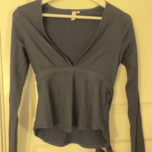 Mörkblå ribbad topp med knytband - Snygg mörkblå topp från Nelly, med v-ringning och långa ärmar. Toppen har ett knytband i midjan för en justerbar passform!