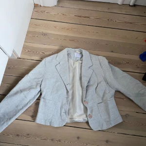 Grå kavaj från Hennes Collection - Snygg grå/beige kavaj från Hennes Collection med klassisk design och två knappar framtill. Perfekt för en stilren look! 