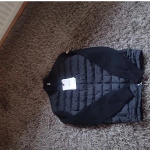 Svart jacka från Moncler - Snygg svart jacka från Moncler med quiltad design och dragkedja. Jackan har långa ärmar och en stilren look, perfekt för kyligare dagar. Moncler-logga på ärmen ger en exklusiv touch.