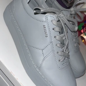 Grå sneakers från Axel Arigato - Snygga grå sneakers från Axel Arigato i skinn med klassisk snörning. Perfekta för en stilren look. Har aldrig används