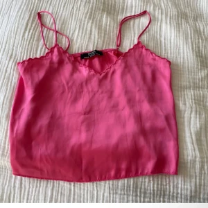 Rosa sidenlinne  - Säljer ett snyggt rosa sidenlinne med tunna axelband och v-ringad kant. Perfekt för sommardagar eller som ett lager under en kavaj. Enkelt och stilrent plagg som passar till många olika outfits.