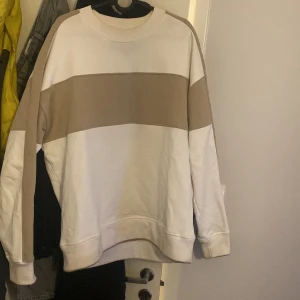 Vit och beige tröja från Moose Knuckles - Säljer en snygg vit och beige tröja från Moose Knuckles. Tröjan har en bred beige rand över bröstet och ärmarna, samt texten 'Moose Knuckles' längs ena ärmen. Perfekt för en stilren och avslappnad look.