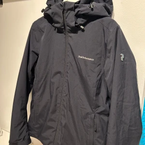 Peak Performance jacka  - Peak performance ”Anima” jacket dam, storlek M och normal i storleken. Väl använd i flera säsonger och har lite tecken på slitningar i tyget men inga hål, fläckar etc. Väldigt väl omhändertagen. Jackan har funktioner som snöskydd, vattentät, vindtät, andningsbar, fodrad, innerficka, armficka och luva. Den är svart i färgen men i vissa ljus kan den se lite marinblå ut. En stor favorit men säljer pga blivit för liten. På peaks egna hemsida är nypris 3500kr och jag säljer för 1800kr.