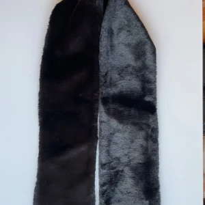 Svart fuskpäls halsduk bredd 14 cm längd 121 cm, i perfekt skick! - Elegant halsduk i svart fuskpäls. Bredd 14 cm längd 121 cm, i perfekt skick! Den har en slät baksida. Ger en mjuk och lyxig känsla.