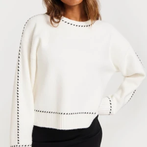 Vit stickad tröja med svarta detaljer - Snygg vit stickad tröja med svarta sömmar längs kanterna. Tröjan har en avslappnad passform och långa ärmar, perfekt för kyligare dagar. Den ribbade nederkanten och ärmsluten ger en stilren look.