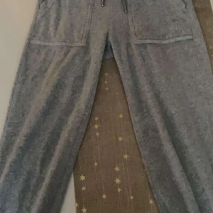 Juicy grå - Säljer ett par grå mjukisbyxor med praktiska fickor framtill. Byxorna har en avslappnad passform och är perfekta för en bekväm dag hemma. De har en elastisk midja med snörning för justerbar passform.