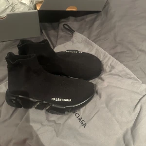 Svarta sneakers från Balenciaga - Snygga svarta sneakers från Balenciaga med en strumpliknande design och vit logotyp på sidan. Skorna har en modern och stilren look med en bekväm sula. Skorna är i storlek 35 men passar 36-37 då dom är stretchiga 