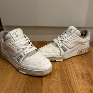 Vita sneakers från Louis Vuitton - Snygga vita sneakers från Louis Vuitton med perforerade detaljer och märkets logotyp på plösen. Skorna har snörning och en unik #54 detalj på hälen. Perfekta för en stilren look. Passar 43-44! Toecap re painted 