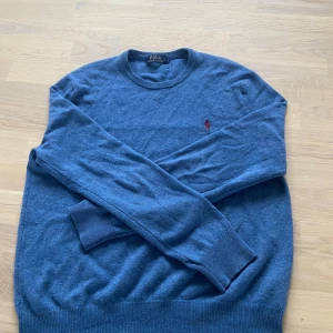 Blå tröja från Polo Ralph Lauren - Snygg blå tröja från Polo Ralph Lauren med rund hals och broderad logga i rött på bröstet. Tröjan har långa ärmar och ribbade muddar vid ärmslut och nederkant. Perfekt för en stilren look! Storlek S, väldigt bra skick😀