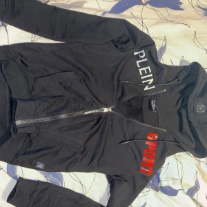 Svart hoodie från Plein Sport - Snygg svart hoodie från Plein Sport med dragkedja och huva. Den har tryck i vitt och rött både fram och bak. Skön hoodie och jäkligt snygg , säljer då den ej passar mig längre 