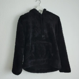 Svart fluffig hoodie från H&M - Mysig svart hoodie från H&M i fluffigt material. Perfekt för kyliga dagar med sin varma och bekväma design. Har en stor ficka framtill och justerbar huva med dragsko.