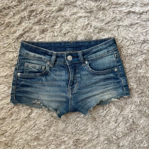 Blå jeansshorts - Snygga blå jeansshorts med fransiga kanter och klassisk femficksdesign. Perfekta för en avslappnad stil. De har en knapp och dragkedja framtill.