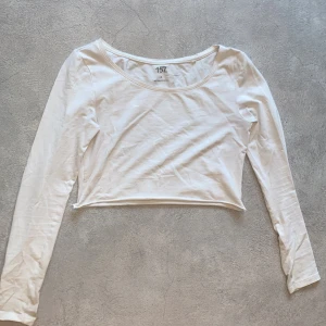 Vit croppad långärmad topp från 157 - Säljer en stilren vit croppad topp från 157. Den har långa ärmar och en rund halsringning, perfekt för en avslappnad look. Toppen är gjord i ett mjukt material som känns skönt mot huden.