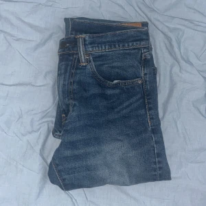 Blå jeans från Levi's - Snygga blå jeans från Levi's med klassisk femficksdesign och en bekväm passform. De har en traditionell knappgylf och är perfekta för en avslappnad stil. Levi's-loggan syns tydligt på baksidan.