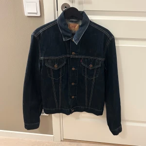 Mörkblå jeansjacka från Levi's - Snygg vintage jeansjacka från Levi's med klassisk design och knappar framtill. Jackan har två bröstfickor med knapp och kontrastsömmar som ger en snygg look. Jackan är min mammas gamla.
