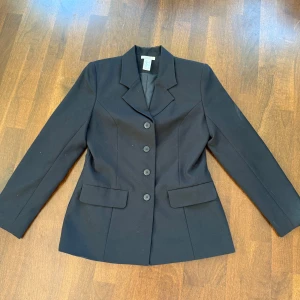 Svart kavaj - Elegant svart kavaj med klassisk design och knäppning framtill. Perfekt för en stilren look. Tillverkad i ett material som ger en fin passform och komfort. Passar utmärkt till både formella och semi-formella tillfällen. Storlek 38 och i super bra skick