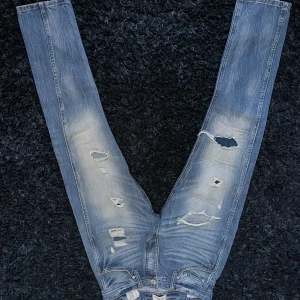 Blå jeans från Jack & Jones - Säljer ett par blå jeans från Jack & Jones med slitna detaljer och en cool, avslappnad look. De är slim jeans och är perfekta för en casual stil. 