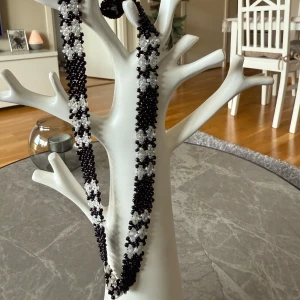 Svart och vitt pärlhalsband - Unikt handgjort halsband med ett vackert mönster av svarta och vita pärlor. Halsbandet har ett blommigt mönster som ger en elegant touch. Perfekt för att lyfta vilken outfit som helst. Aldrig använt.