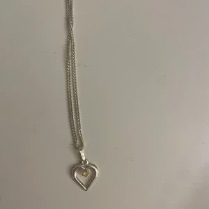 Silverhalsband med hjärthänge - Elegant silverhalsband med ett hjärthänge som har en liten gul detalj i mitten. Perfekt för att ge en subtil men stilfull touch till din outfit. Halsbandet är i äkta silver 