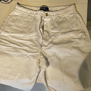 Vita shorts från Polo Ralph Lauren - Snygga vita shorts från Polo Ralph Lauren med dragkedja och knapp framtill. Klassisk design med fickor både fram och bak, perfekta för en stilren look. Passar utmärkt till varma dagar.