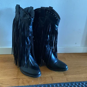 Svarta boots med fransar - Snygga svarta boots med långa fransar och nitar upptill. Perfekta för en cool och unik stil. De har en spetsig tå och är tillverkade i syntetmaterial. Aldrig använda.