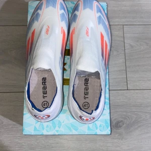 ADIDAS F50 ELITE LACELESS FG ADVANCEMENT - VIT/RÖD/LUCID BLUE - Helt nya ADIDAS F50 ELITE LACELESS FG ADVANCEMENT - VIT/RÖD/LUCID BLUE.  Perfekta för fotbollsplanen med sina greppvänliga dobbar.oanvänd med kartong. 
