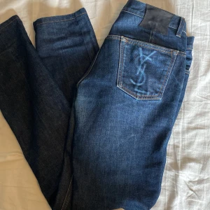 Blå jeans från Yves Saint Laurent - Snygga blå jeans från Yves Saint Laurent med tight passform. De har en klassisk femficksdesign och ett YSL-märke på bakfickan. Perfekta för en stilren look. Modellen på bilderna är 180 70 kg