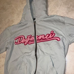 Ljusgrå hoodie med rosa text grönaktig tröja - Säljer en ljusgrå hoodie med huva och dragkedja framtill. Den har en stor rosa text på bröstet. Perfekt för en avslappnad stil.