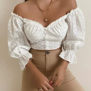 Zara strl M Vit offshoulder blus med prickigt mönster - Säljer en söt vit offshoulder blus från Zara med prickigt mönster och knappar framtill. Blusen har långa ärmar med volangdetaljer vid ärmslut och en croppad passform. Perfekt för sommarens varma dagar! Passar S/M