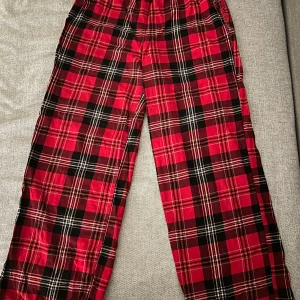 Röda rutiga byxor från Victoria's Secret - Snygga röda byxor med klassiskt rutigt mönster från Victoria's Secret. Perfekta för en avslappnad stil med en elastisk midja för extra komfort. Tillverkade i mjukt material som känns skönt mot huden.