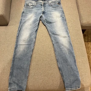 Blå jeans från Replay - Snygga blå jeans från Replay, modell Anbass. De har en klassisk femficksdesign och en lätt slitning på framsidan för en cool look. Perfekta för en avslappnad stil.