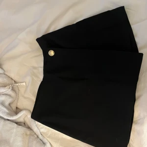 Svart shorts kjol med knappdetalj - Snygg svart shorts kjol med en stilren knappdetalj framtill. Aldrig använd 