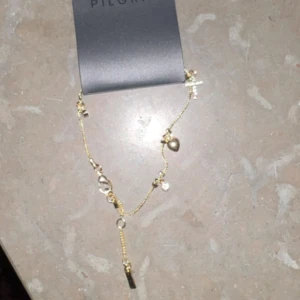 Guldarmband med berlocker från Pilgrim - Elegant guldarmband från Pilgrim med flera berlocker, inklusive hjärtan och små stenar. Perfekt för att lägga till en touch av glamour till din outfit. Armbandet har en justerbar kedja för perfekt passform.