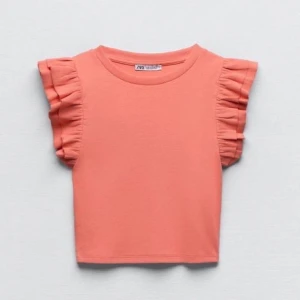 Korallfärgad topp med volangärmar från Zara - Snygg korallfärgad topp från Zara med volangdetaljer på ärmarna. Perfekt för en somrig look. Toppen är croppad och har en rund halsringning.