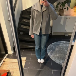 Grå kappa med knappar - Säljer en stilren grå kappa. Jackan har en klassisk design och är perfekt för kyligare dagar. Den har långa ärmar och en rak passform som ger en elegant look. Är i young ginas kollektion strl170 som motsvarar S