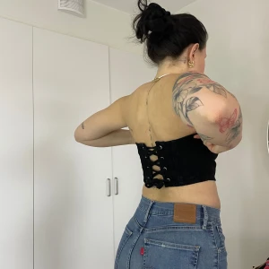 Svart tubtopp med snörning och blixtlås - Snygg svart tubtopp med snörning i ryggen. Perfekt för en trendig look. Toppen är axelbandslös och har en stilren design. 