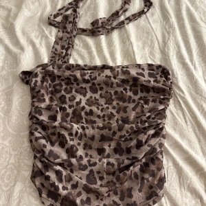 Leopardmönstrad axelväska - Snygg leopardmönstrad topp med rynkade detaljer. Perfekt för att ge din outfit en vild touch. Toppen har en scarf som man kan ha med toppen om man vill! 