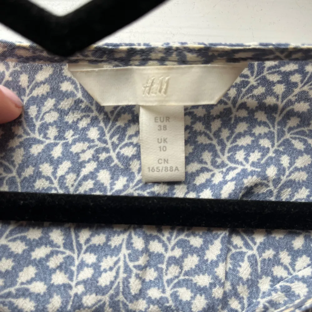 Säljer en söt blommig blus från H&M i blått och vitt. Blusen har korta ärmar och en v-ringad design med knytning framtill. Perfekt för en avslappnad stil med en liten volangdetalj vid nederkanten. 💙🪻🤍. Puserot.