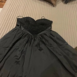 Satin lace babydoll mini dress från Boohoo. Storlek: XXXL - Snygg svart babydoll-klänning från Boohoo i satin med spetsdetaljer. Klänningen har en vacker v-ringning och tunna axelband. Perfekt för en elegant look. Aldrig använd. Lapp finns kvar på klänning. Säljer för 350 kronor 