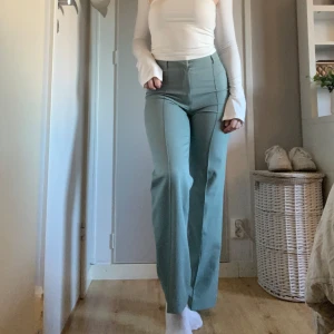 Ljusgröna kostymbyxor  - Högmidjade gröna kostymbyxor med veckade detaljer från madlady. I storlek 32 (midja rakt över 33 cm) och  (innerben 76 cm). Har tecken på användning då dessa är köpta second hand men säljer då de aldrig kommit till användning🎀