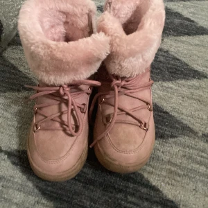 Rosa boots med fuskpäls - Säljer ett par rosa boots med mjuk fuskpäls och snörning. Perfekta för kalla dagar med sin varma insida och robusta sula. De har en snygg design med detaljer i metall och en bekväm passform.