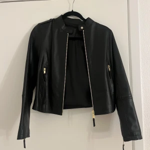 Svart skinnjacka från Massimo Dutti - Snygg svart skinnjacka från Massimo Dutti med dragkedja och stilrena detaljer. Jackan har en kortare passform och långa ärmar, perfekt för en trendig look. Köpt för 2000kr, aldrig använd men lappar är borttagna