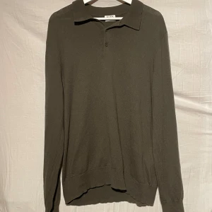 Olivgrön tröja från Filippa K - Snygg olivgrön tröja från Filippa K med krage och knappar framtill. Perfekt för en stilren look. Tröjan har långa ärmar och är tillverkad i ett mjukt material.