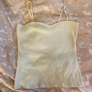 Beige ribbad linnetopp från Gina Tricot - Säljer en stilren beige ribbad linnetopp från Gina Tricot. Toppen har smala axelband och en figurnära passform som ger en snygg siluett. Perfekt för varma dagar eller som ett lager under en kavaj.
