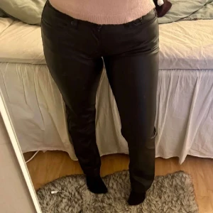 Svarta byxor i syntetmaterial - Snygga svarta byxor i syntetmaterial med en tight passform. Perfekta för en stilren look. De har en klassisk design med dragkedja och knapp framtill. Går ej att köpa på hemsidan länge. 