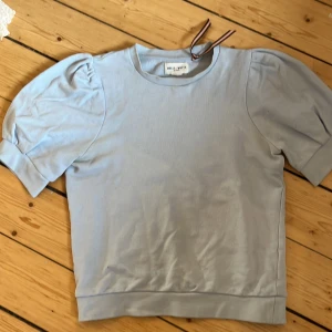 Ljusblå tröja från Holly & Whyte - Säljer en ljusblå tröja från Holly & Whyte. Tröjan har korta puffärmar och en rund halsringning. Perfekt för en stilren och bekväm look.