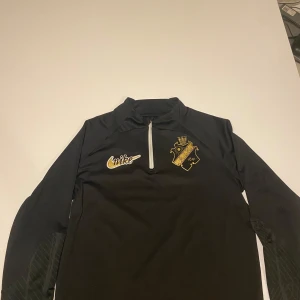 NIKE DRILLTOP GULDDETALJER - HERR - Säljer en svart långärmad tröja från Nike med AIK-logga på bröstet. Tröjan har en dragkedja vid halsen och är i Dri-FIT material för optimal komfort. Perfekt för fotbollsfans och träning. Skriv ett PM för bilder,mått,byten,pris