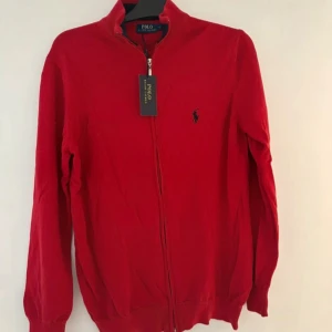Ralph Lauren full zip - Snygg röd tröja från Polo Ralph Lauren med dragkedja och klassisk krage. Tröjan har långa ärmar och en liten broderad logga på bröstet. Helt ny med prislapp på och köpt för 1999kr:)
